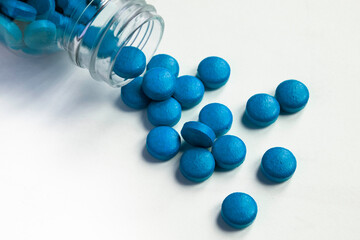 Blue pills and tablets spilling out from glass pill bottle on white background