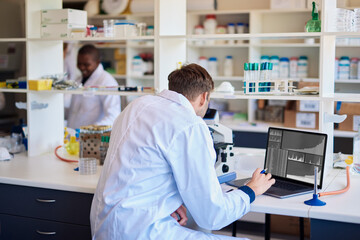 Male technician working with a microscope and laptop in a lab