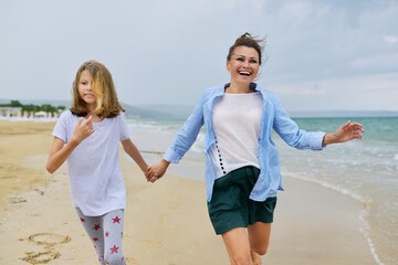 Happy mom and daughter running on the sea beach holding hands