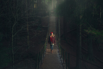 The girl walks on a suspension bridge over a mountain river.