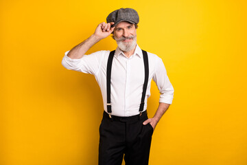 Photo of mature man happy positive smile hand touch retro hat suspenders isolated over yellow color background