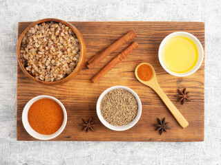 Buckwheat in ceramic bowl, cumin, cinnamon, star anise, oil, red pepper chili on white concrete background