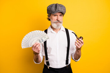 Photo of aged man serious hold smoke pipe tobacco dollars banknotes cash rich money isolated over yellow color background