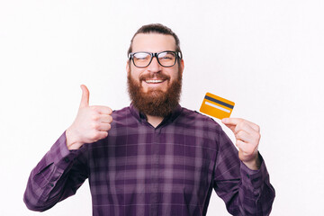Portrait of handsome man wearing eyeglasses holding credit card and showing thumb up