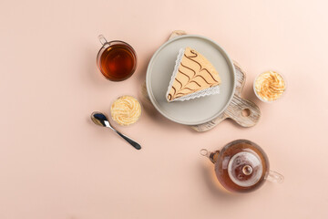 A piece of cheesecake on a plate with a teapot and a cup of tea on a colored background. A delicious dessert for a birthday and holiday.