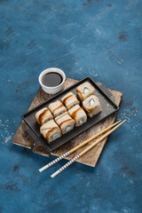 Asian food-eel and cheese rolls on a plate with chopsticks and soy sauce on a light blue background