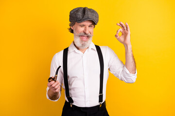 Photo portrait of gentleman winking keeping wooden pipe showing ok gesture isolated vibrant yellow...