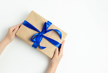 Gift box with a blue ribbon in the hands of a child on a white background. Fathers day, birthday and holiday concept. Top view, flat lay, copy space