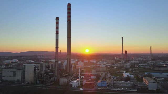 Aerial: Oil petrochemical industrial site during sunset. Chimneys of power plant refinery at sunrise polluting environment concept