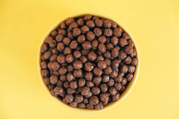 Chocolate cereal corn balls in a yellow bowl on a yellow background. Top view. Copy, empty space for text