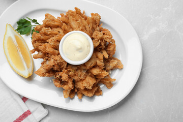Delicious onion blossom served with lemon and sauce on white table, flat lay