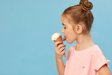 cute little girl eating vanilla ice cream in a waffle cone on blue background. copy space for text