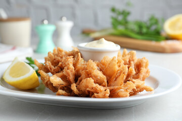 Delicious onion blossom served with lemon and sauce on white table