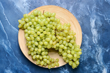 Plate with ripe green grapes on color background