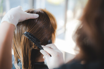 Hairdresser putting mask and coloring on woman's hair in beauty salon, Professional hairdresser dyeing hair of her client, Process of dyeing hair at beauty salon