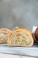 Cut in half croissant with inside texture and thin crisp layers on wooden board, light concrete background. Delicious french pastry.
