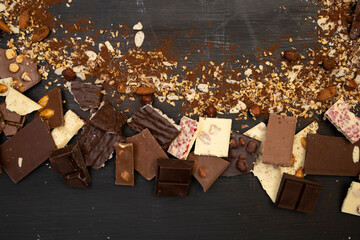 a lot of different types of chocolate and various ingredients such as nuts and cocoa powder lie on a black wooden plate photo taken from above