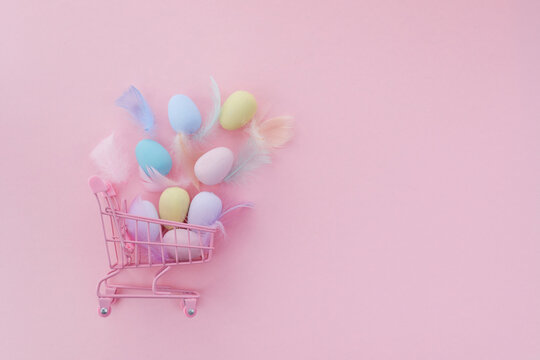 Easter sale background. Shopping cart with colorful easter eggs on pink background.