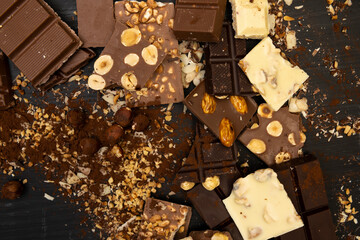 a lot of different types of chocolate and various ingredients such as nuts and cocoa powder lie on a black wooden plate photo taken from above