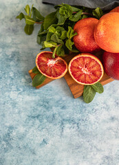 Sliced and whole ripe juicy Sicilian blood oranges on wooden cutting board with mint, blue concrete...