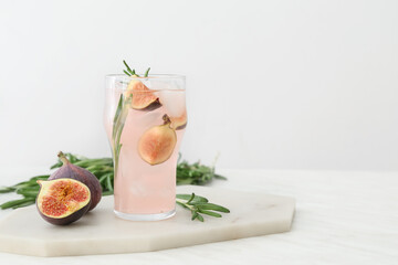 Board with glass of tasty fig lemonade on light background