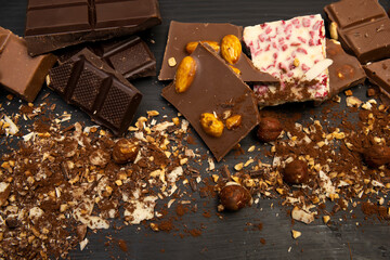 a lot of different types of chocolate and various ingredients such as nuts and cocoa powder lie on a black wooden plate photo taken from above
