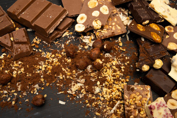 a lot of different types of chocolate and various ingredients such as nuts and cocoa powder lie on a black wooden plate photo taken from above