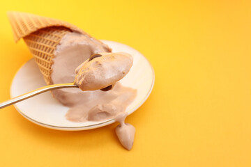 Melted chocolate ice cream in a teaspoon on the background of a saucer with ice cream on a yellow background, close-up
