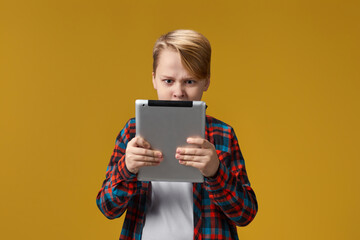 angry child boy in checkered shirt using digital tablet on yellow background