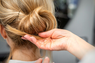 Fototapeta premium Close up of hands of female hairdresser styling hair of a blonde woman in a hair salon