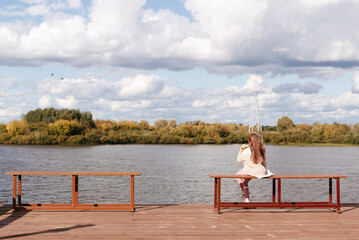 little girl sitting on a bench near the water and eating a bun back view