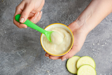 Woman holding bowl with healthy baby food on dark background, closeup