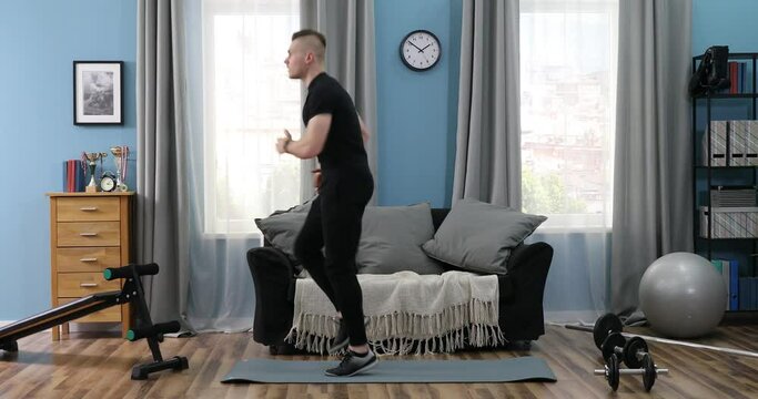 Handsome Young Man in a Black T-Shirt and black gym suit doing stretching at home. Handsome Guy doing warm up in Living Room at Home. Sports at Home Online. Athlete exercising and doing workout