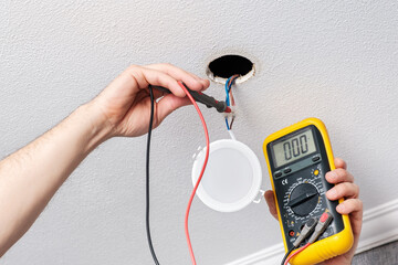 Electrician hands measure with tester power supply voltage before installing modern LED light bulb...