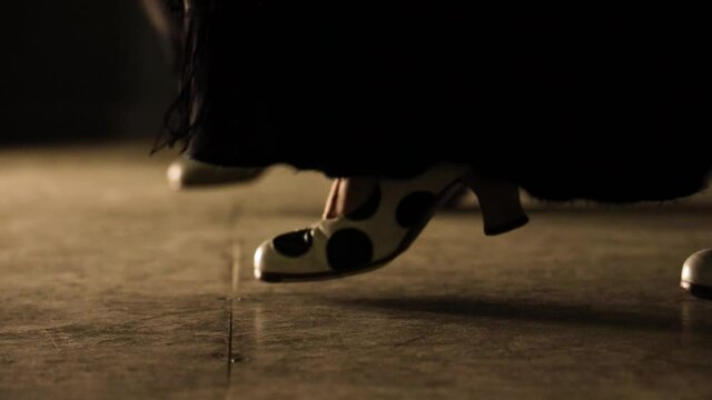 closeup of two women flamenco shoes with black skirt dress dancing on a wooden floor