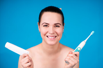 Portrait of happy beautiful girl, young woman smiling and showing her white teeth, holding electro electric toothbrush and tube of toothpaste. Health care, hygiene, oral, dental beauty concept