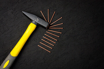 a black, yellow and gray hammer and thin nails on black background - Powered by Adobe