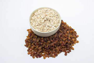 Oatmeal and raisins on a white background. Healthy diet. A full cup of oatmeal, raisins scattered nearby. The concept of proper nutrition