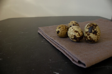 Quail eggs lie on a napkin on a dark background, behind a white background. 