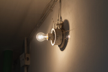 An incandescent light bulb with cobwebs and dirt illuminates the white wall in the entrance of the house