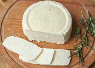 homemade cheese young white circle lies on a wooden board, cut into slices