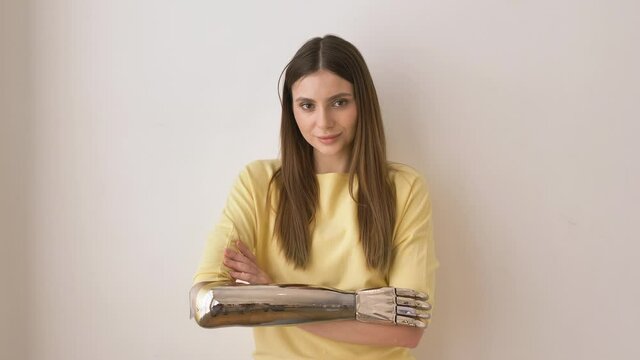 Cheerful long haired lady with contemporary bionic arm in yellow shirt poses for camera on beige wall background closeup