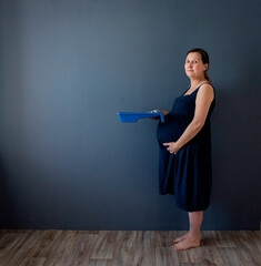 Pregnant woman in a blue dress against a white wall makes repairs, dreams, selective focus