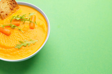 Bowl of tasty carrot cream soup on color background, closeup