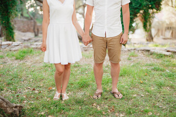 Man and woman stand side by side in the park on the grass and hold hands 