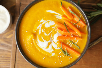 Bowl of tasty carrot cream soup on wooden background, closeup