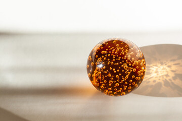 orange glass ball with air bubbles inside illuminated by sunlight on a white-gray background
