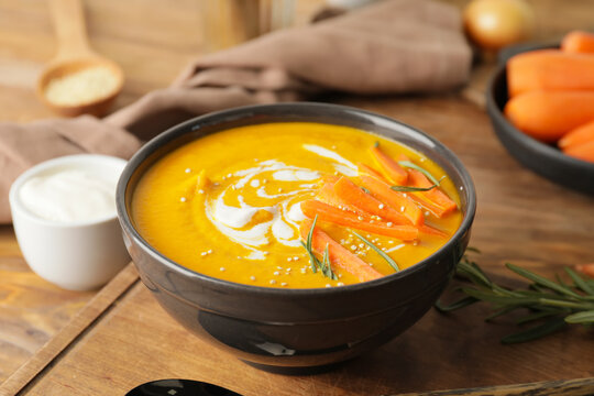 Bowl of tasty carrot cream soup on wooden background, closeup