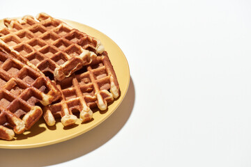 Traditional Belgian dessert. Freshly baked Belgian waffles with sugar on yellow plate isolated over light background