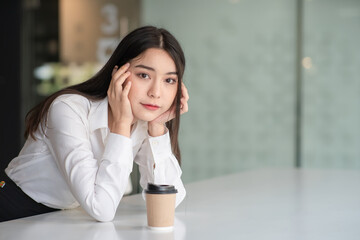 Fototapeta premium Portrait of a charming smiling young woman sitting near the window with a cup of hot coffee and looking at the camera.